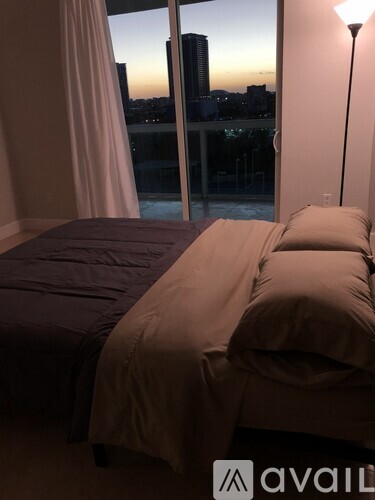 A bedroom with a large bed and a view of the city at dusk.