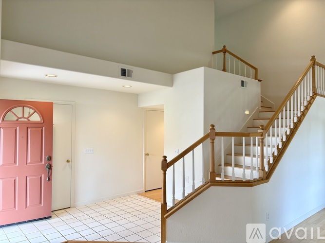 A pink door is on the left of a white hallway.