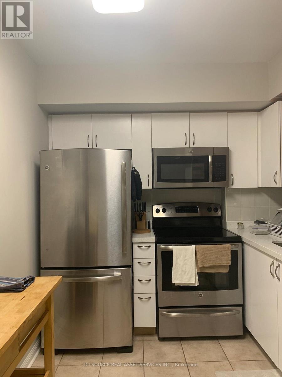 A kitchen with a stainless steel refrigerator, microwave, oven, and white cabinets.