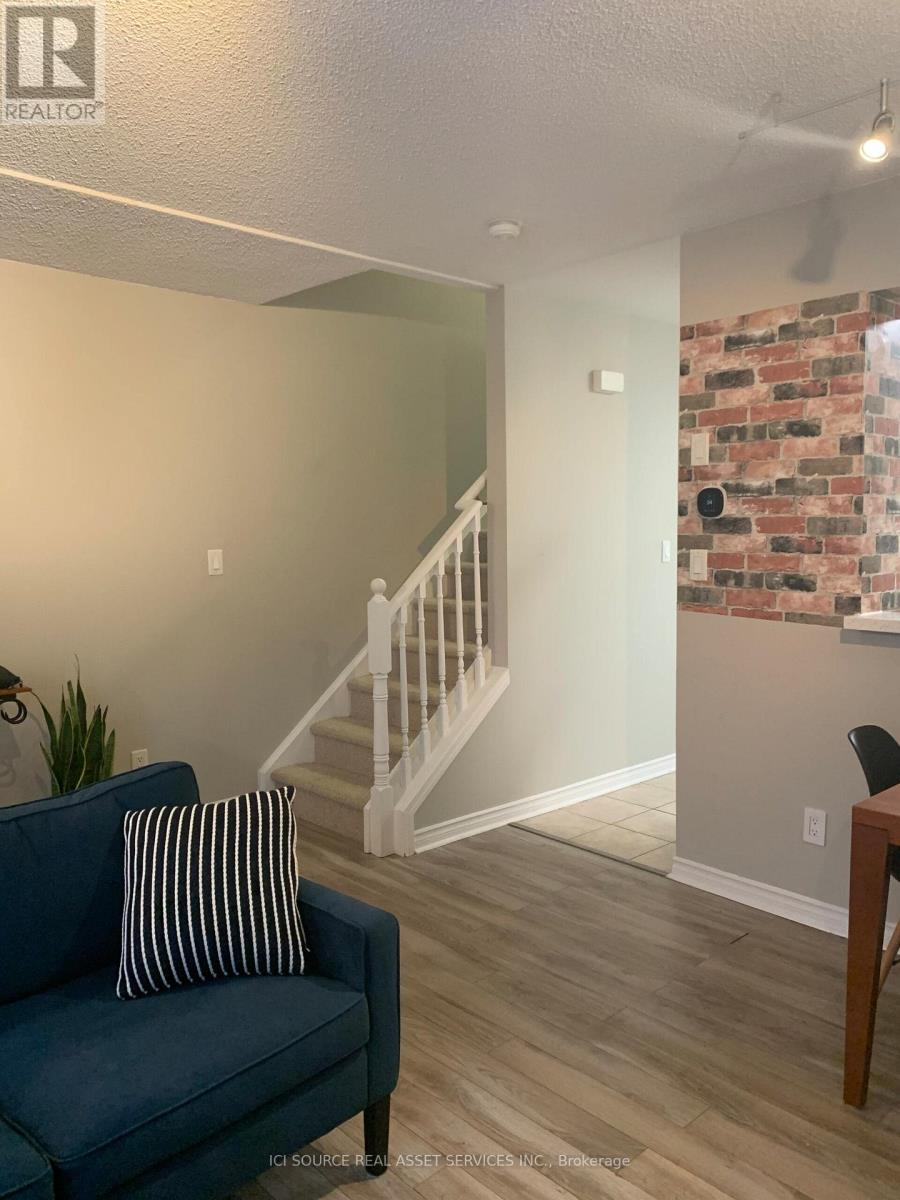A blue couch with a striped pillow sits in a room with a brick wall and a staircase.