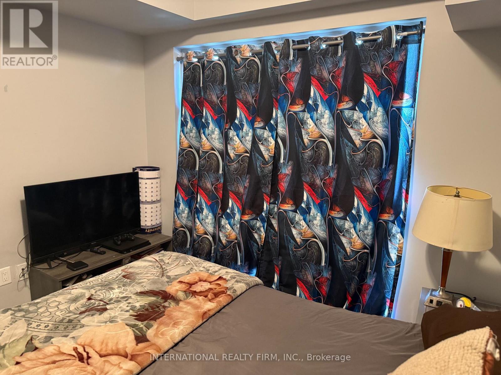 A bedroom with a bed, a television, a lamp, and a curtain with a pattern of red, white, and blue.