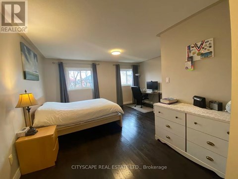 A bedroom with a bed, dresser, and desk with a lamp on the nightstand.