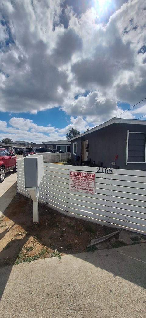 A red car is parked in a lot behind a fence with a sign that says "No Parking".