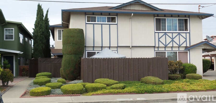 A house with a white and blue exterior is surrounded by a brown fence and green bushes.