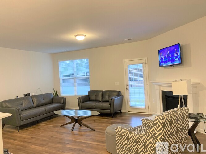 A living room with a grey couch, a black leather chair, a patterned armchair, and a television mounted on the wall.