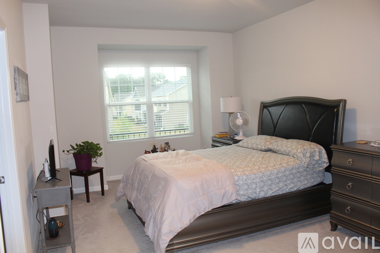 A bedroom with a large bed, a nightstand, and a window with blinds.