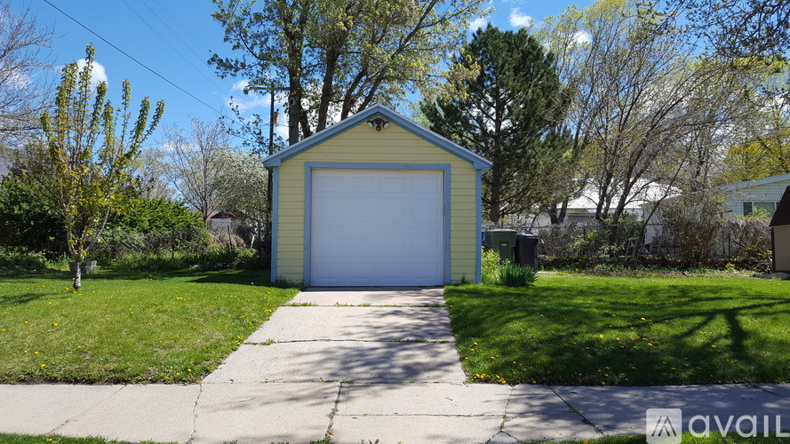 A small garage with a white door is surrounded by a grassy area and trees.