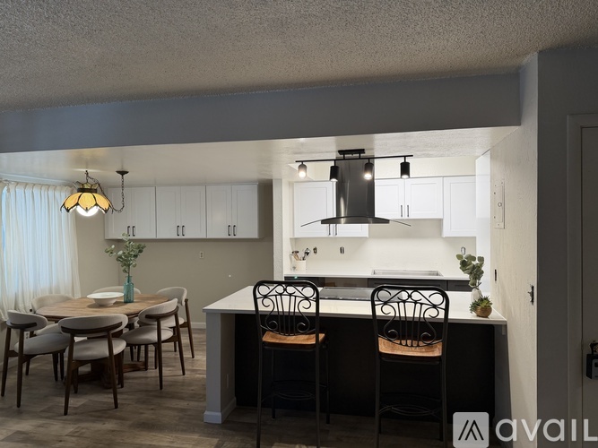 A kitchen with a table and chairs in the foreground and a counter with a sink and a hanging light fixture above it.