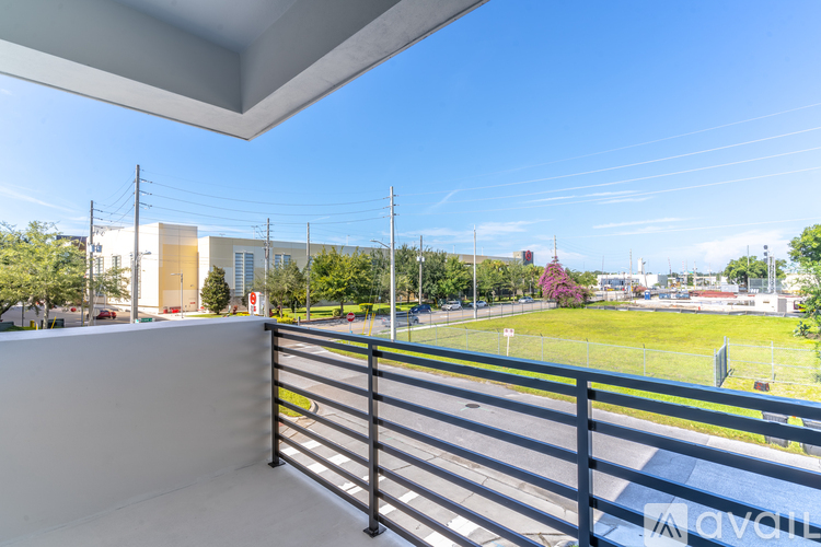 A balcony with a metal railing overlooks a green field and buildings.