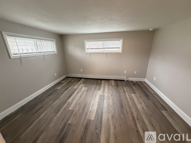 A room with wooden flooring and two windows.