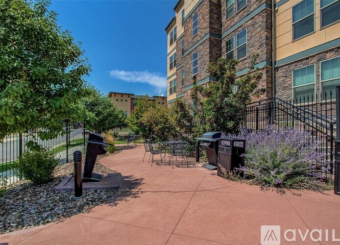 A walkway with a metal railing and a bench is surrounded by greenery and a building.