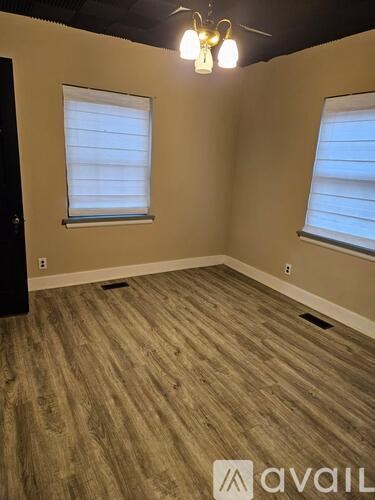 A room with wooden flooring and two windows.