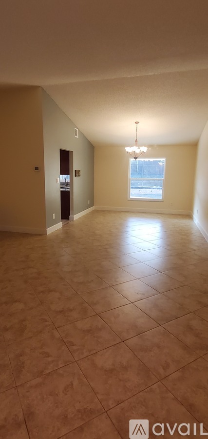 A spacious room with tiled flooring and a chandelier hanging from the ceiling.