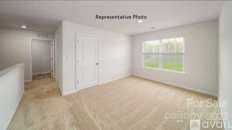 A room with a carpeted floor and a window showing a fence and trees outside.