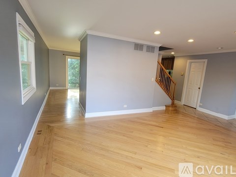 A spacious room with wooden flooring and a staircase in the background.