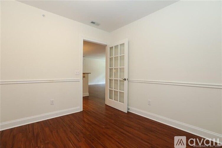 A room with wooden floors and white walls, with a doorway leading to another room.