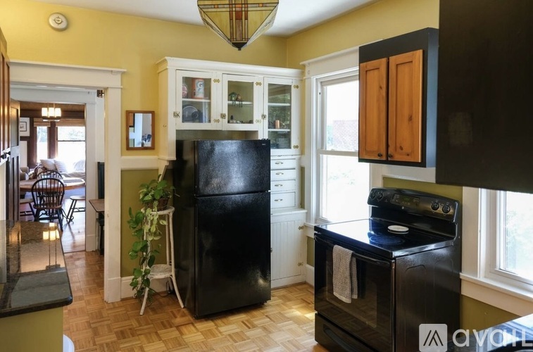 A black refrigerator stands in a kitchen with wooden floors and white cabinets.