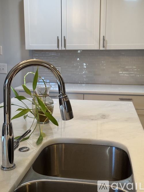 A kitchen sink with a silver faucet and a vase with green leaves on the counter.