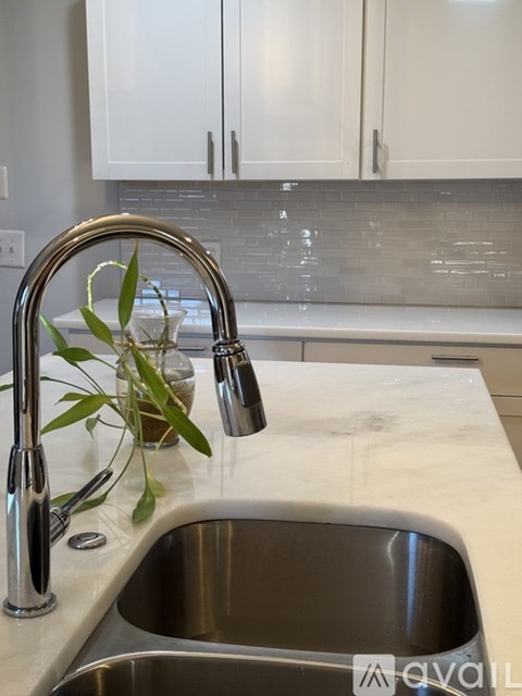 A kitchen sink with a silver faucet and a vase with green leaves on the counter.