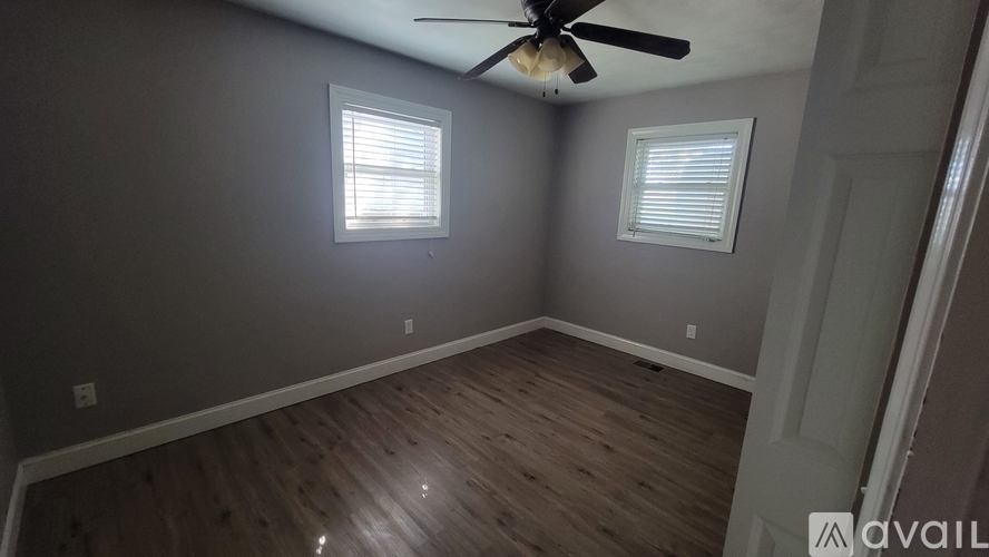 A room with a ceiling fan and two windows.