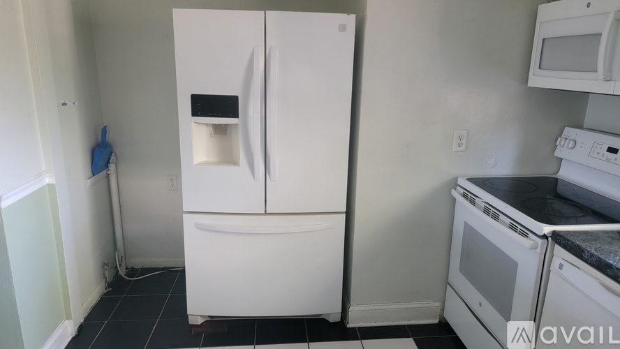 A white fridge with a black handle sits in a kitchen with a white oven and microwave.