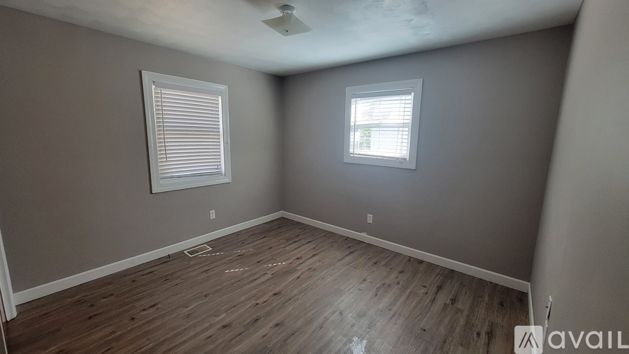 A room with wooden flooring and two windows.