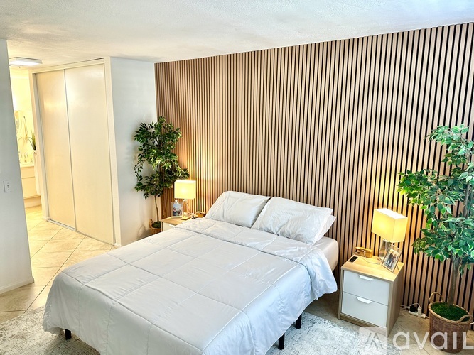 A bedroom with a bed, nightstand, and two potted plants.