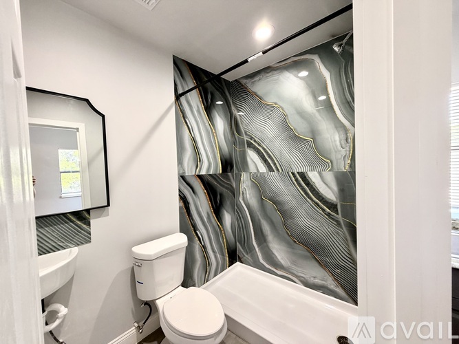 A bathroom with a toilet, a bathtub, and a shower curtain with a grey and black design.