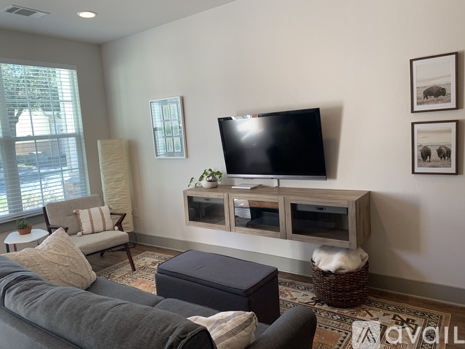 A living room with a grey couch, a television, and a window with blinds.