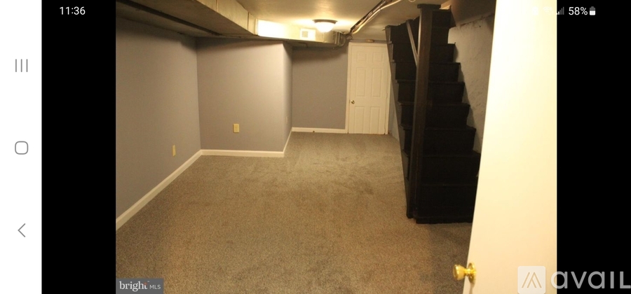 A room with carpeted floor and a staircase on the right side.