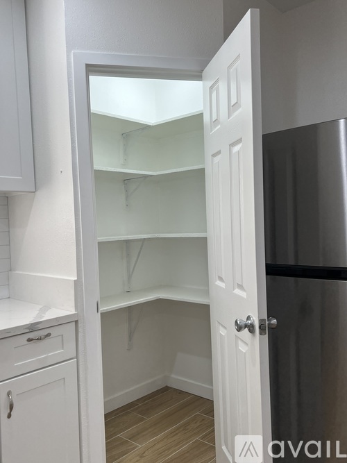 A white door is open to a kitchen with a black fridge.