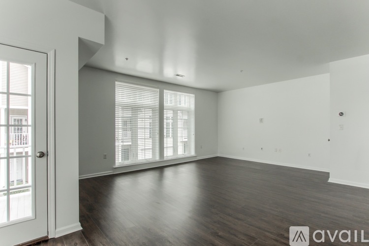 A spacious room with wooden floors and a large window with blinds.