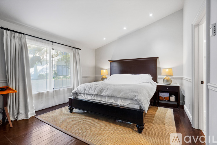 A bedroom with a large bed and a window with curtains.