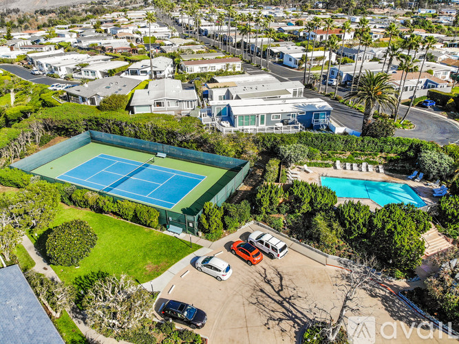 A tennis court is surrounded by a green fence and a pool.