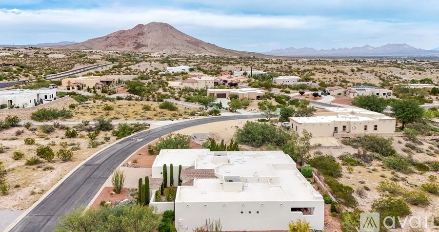 A white building is situated in the desert with a mountain in the background.