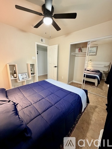A bedroom with a bed covered in a blue comforter and a ceiling fan.