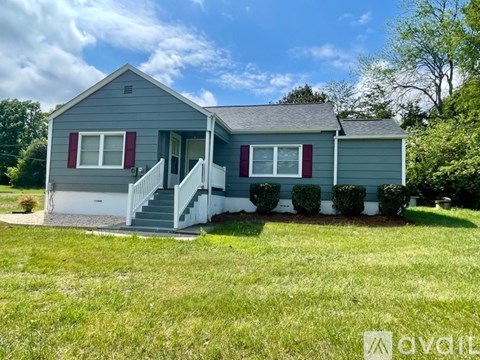 A house with a grey siding and red shutters is for sale.