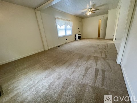 A spacious room with a carpeted floor and a ceiling fan.