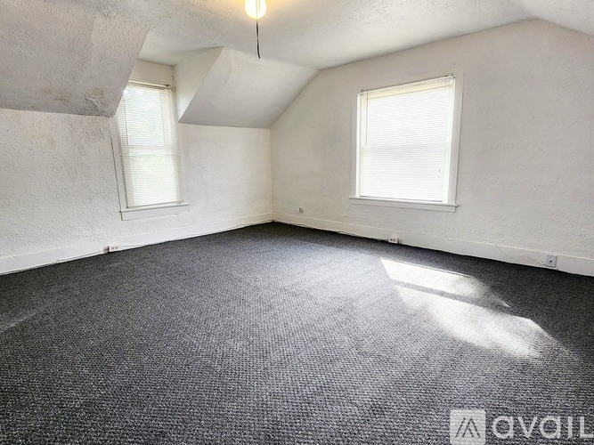 A room with a grey carpet and two windows.