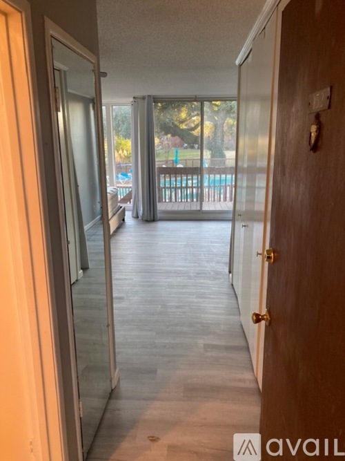 A hallway with a wooden door leading to a balcony with a pool.