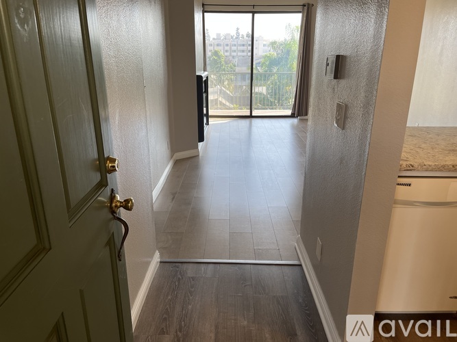 A hallway with a door on the left and a window with a view of a city on the right.