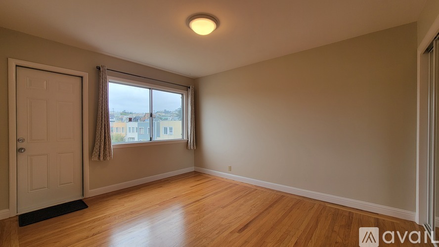 A room with wooden floors and a large window with a view of buildings outside.