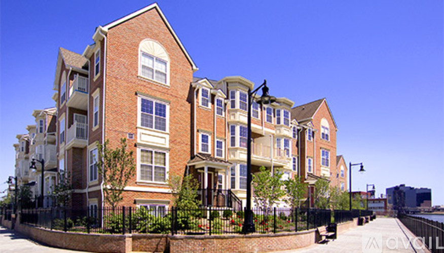 A row of red brick apartment buildings with black fencing and green trees in front.