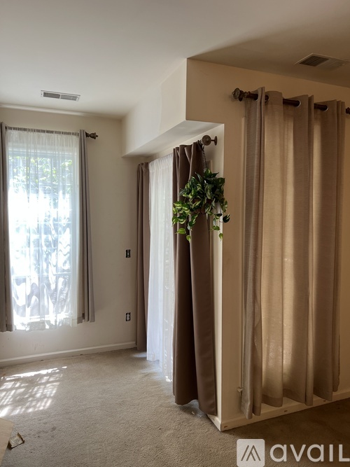 A room with a carpeted floor, a window with white curtains, and a brown curtain.