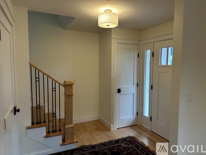 A hallway with a staircase and a rug on the floor.
