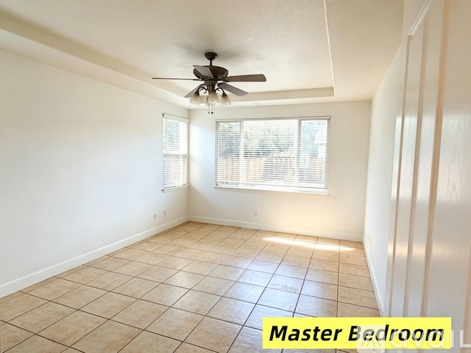 A master bedroom with a ceiling fan and tiled floor.