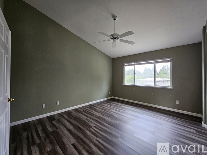 A room with a ceiling fan and a window with a view of trees.