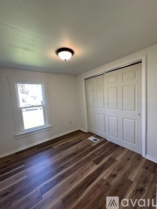 A room with a white door, a window, and wooden flooring.
