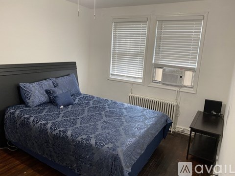 A bed with a blue patterned cover sits in a room with a window and a radiator.