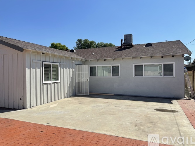 A house with a grey exterior and a brick driveway is available for rent.